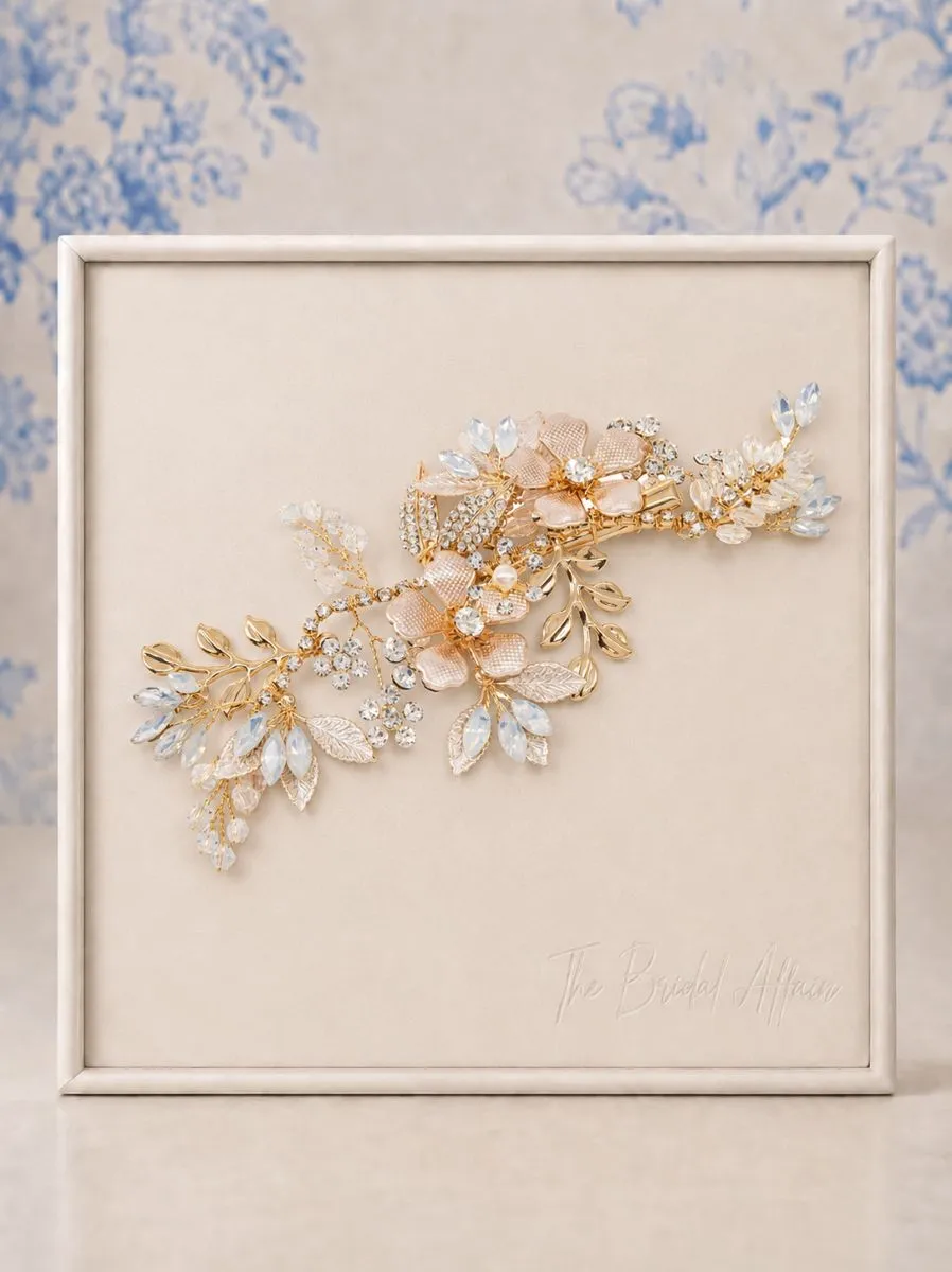 7799 Exquisite Pink Blush Headpiece - Athena Athena 7799 Exquisite Pink Blush Headpiece. Bring enchantment to your day with this alluring headpiece. Embellished with pink blush flowers cocooned amongst a lush variety of crystal embellished flowers, simulated pearls and crystals. An intricate finish to bring harmony and sweetness to your look. Details; High quality crystals. hand painted pink blush flowers, simulated ivory pearls and clear crystal beads. High shine gold finish. Dimensions : 19cm x 7.5cm wide. Fitted with a crocodile clip at the back.