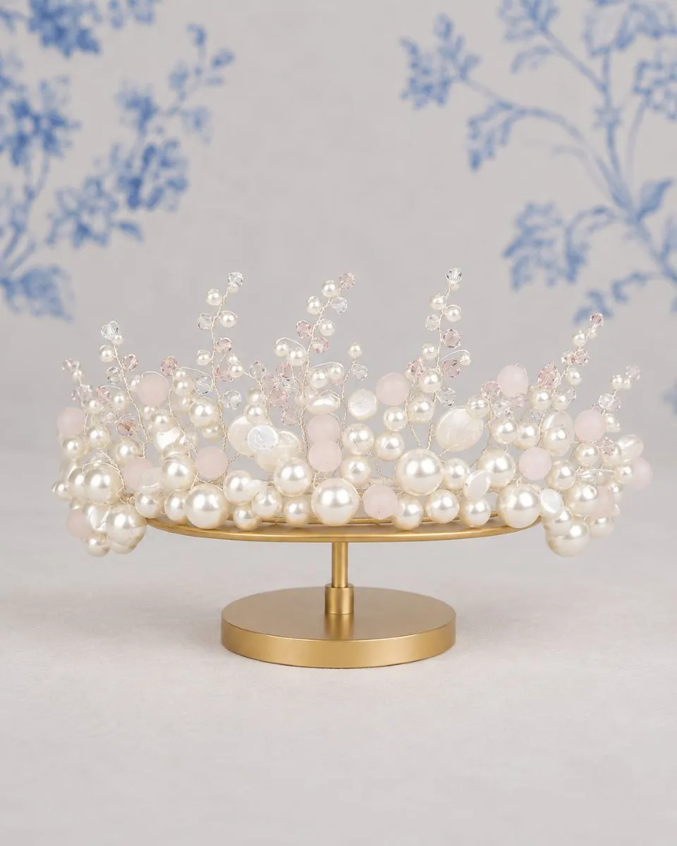 TR2818A Pearl and Crystal Crown by Richard Designs in blush pink on a gold stand against blue floral backdrop.