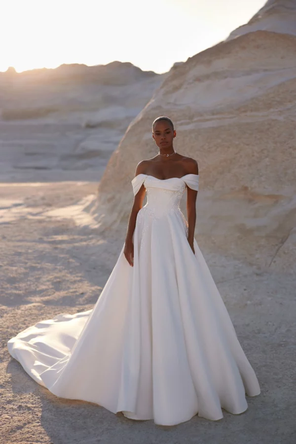 Eva Lendel Chabli wedding dress full view &ndash; off-shoulder satin ball gown with corset bodice and long train in desert setting