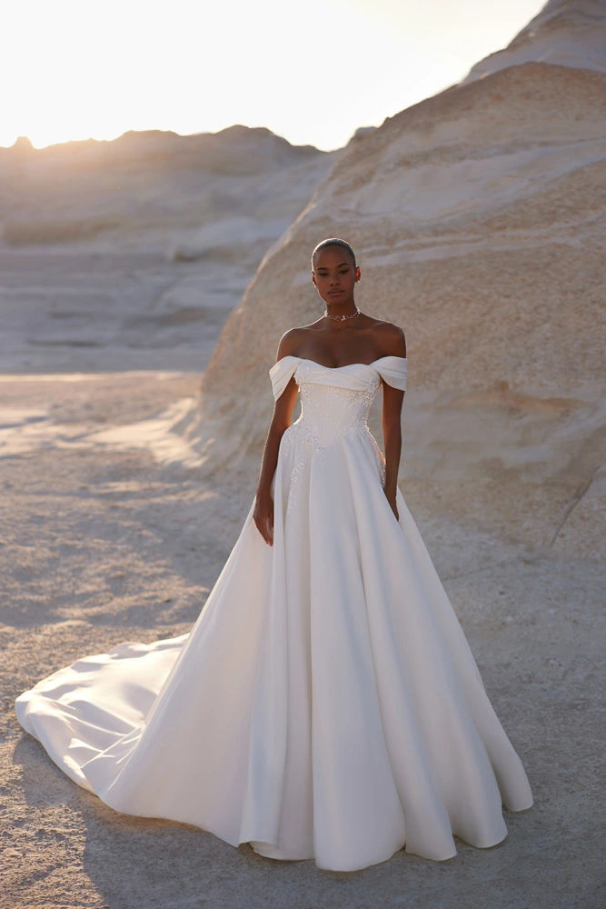 Eva Lendel Chabli wedding dress full view &ndash; off-shoulder satin ball gown with corset bodice and long train in desert setting