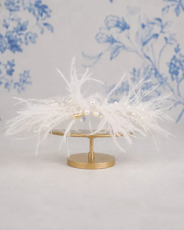 TR2817A Ortega Feather Crown by Richard Designs with ostrich feathers, pearls and crystals on gold stand against blue floral backdrop.