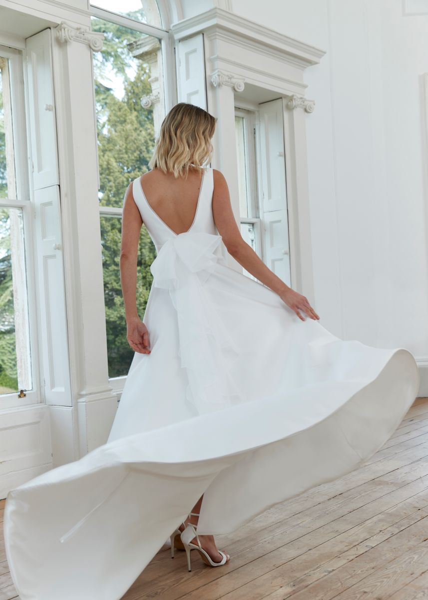 Romantica of Devon Dawn wedding dress back view showing low V-back and flowing satin skirt with detachable organza bow