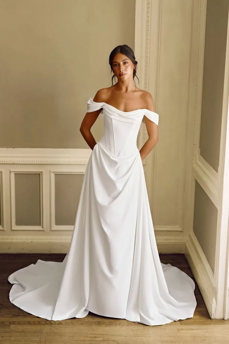 Elodie by Phoenix Gowns ivory crepe A-line wedding dress with draped off-the-shoulder neckline, structured basque waist and flowing skirt.