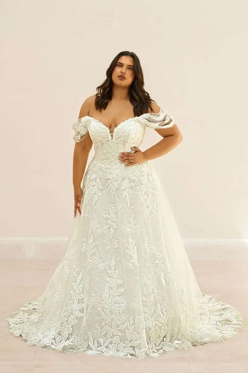 Elysanne by Envy by Phoenix Gowns ivory lace A-line wedding dress with flowing skirt and delicate leafy appliqu&eacute;s.
