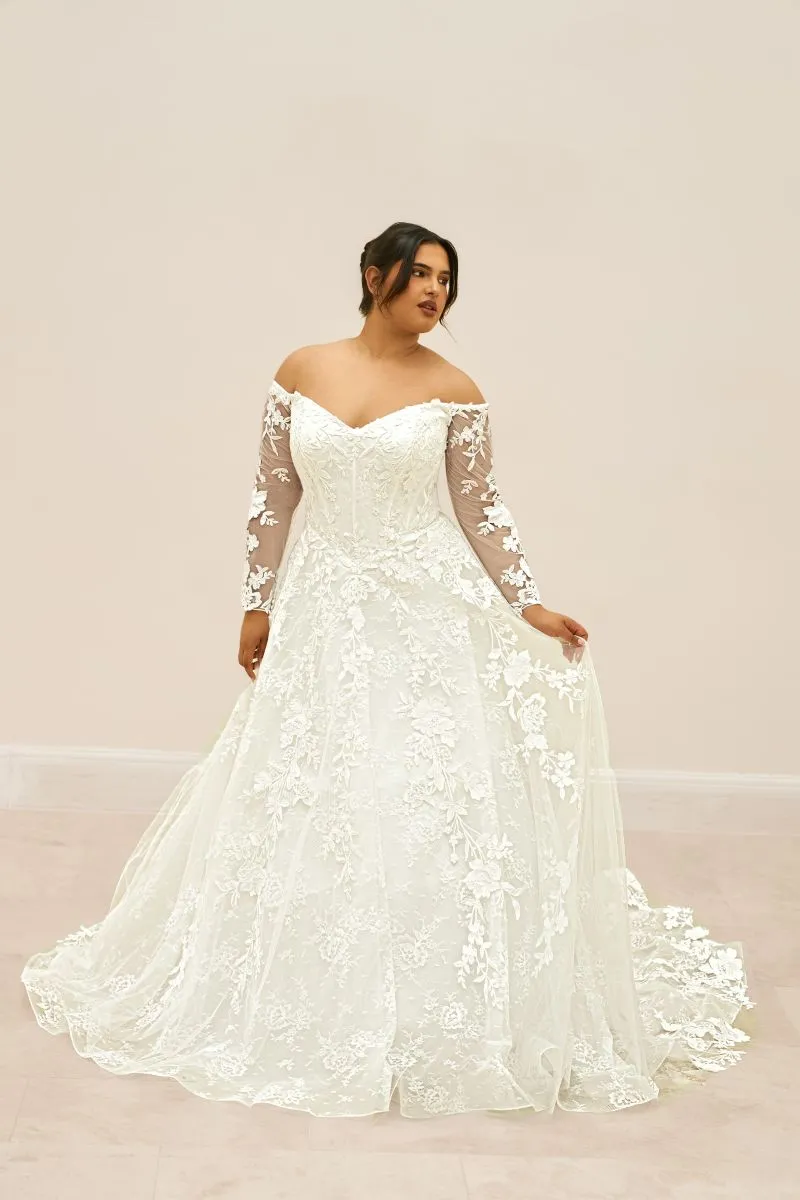 Full-length front view of Evania by Envy by Phoenix Gowns, an ivory A-line lace wedding dress with long sleeves and flowing floral lace skirt.